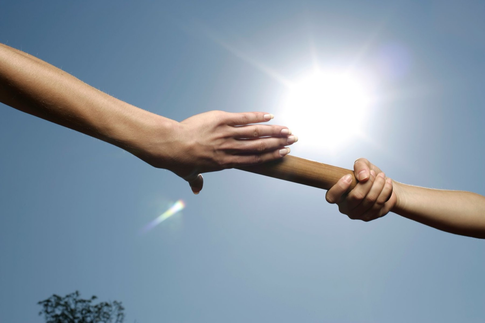 One hand passing a baton to another in the sunlight